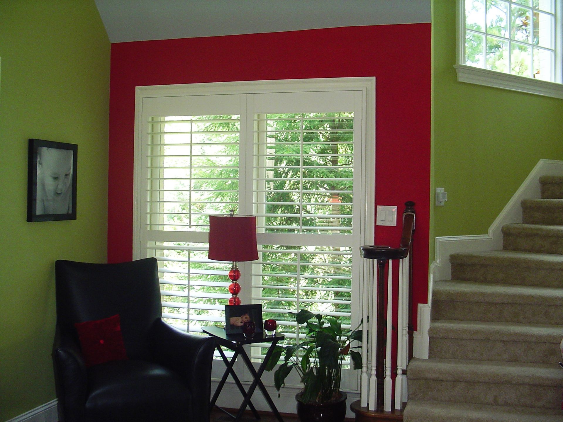 Interior room with lime green and red walls, white shutters, black chair, and staircase.