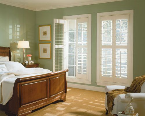 Bedroom with a wooden bed, white shutters on windows, and a green wall.