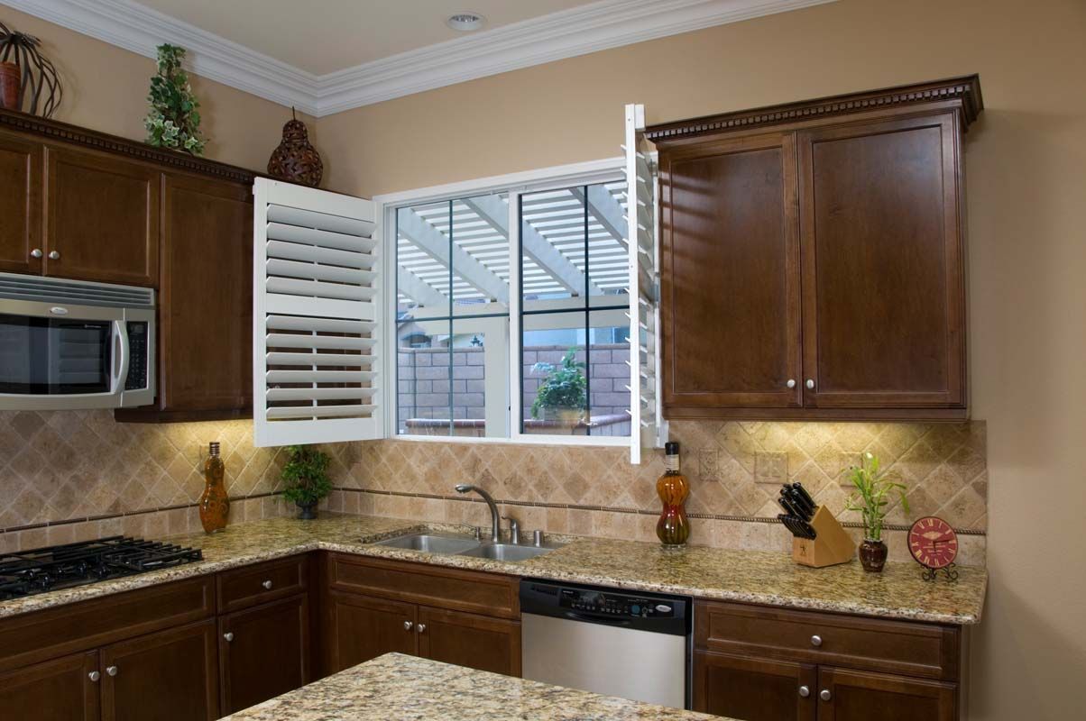 Kitchen with brown cabinets, granite countertops, and white shutters open over a window.