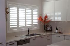 White kitchen with window shutters, sink, countertop, and cabinets.