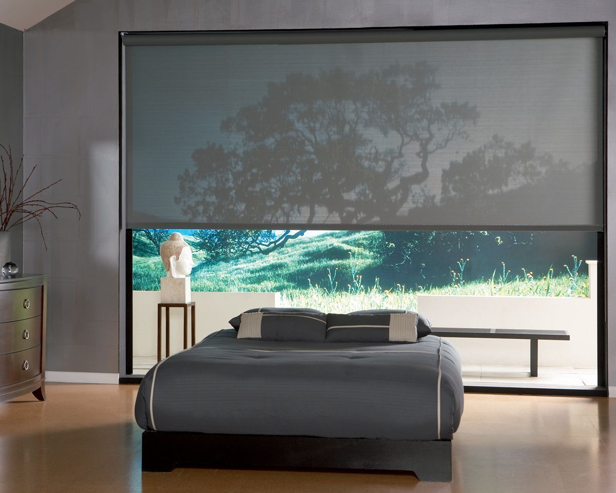 Bedroom with large window, bed, and sheer shades; view of outside trees.