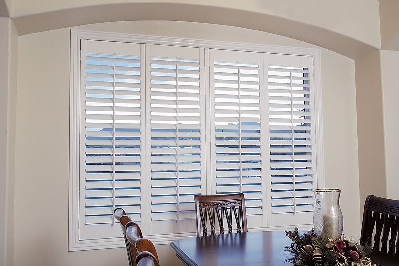 White shuttered windows in a dining room, with a partially visible table and chairs.