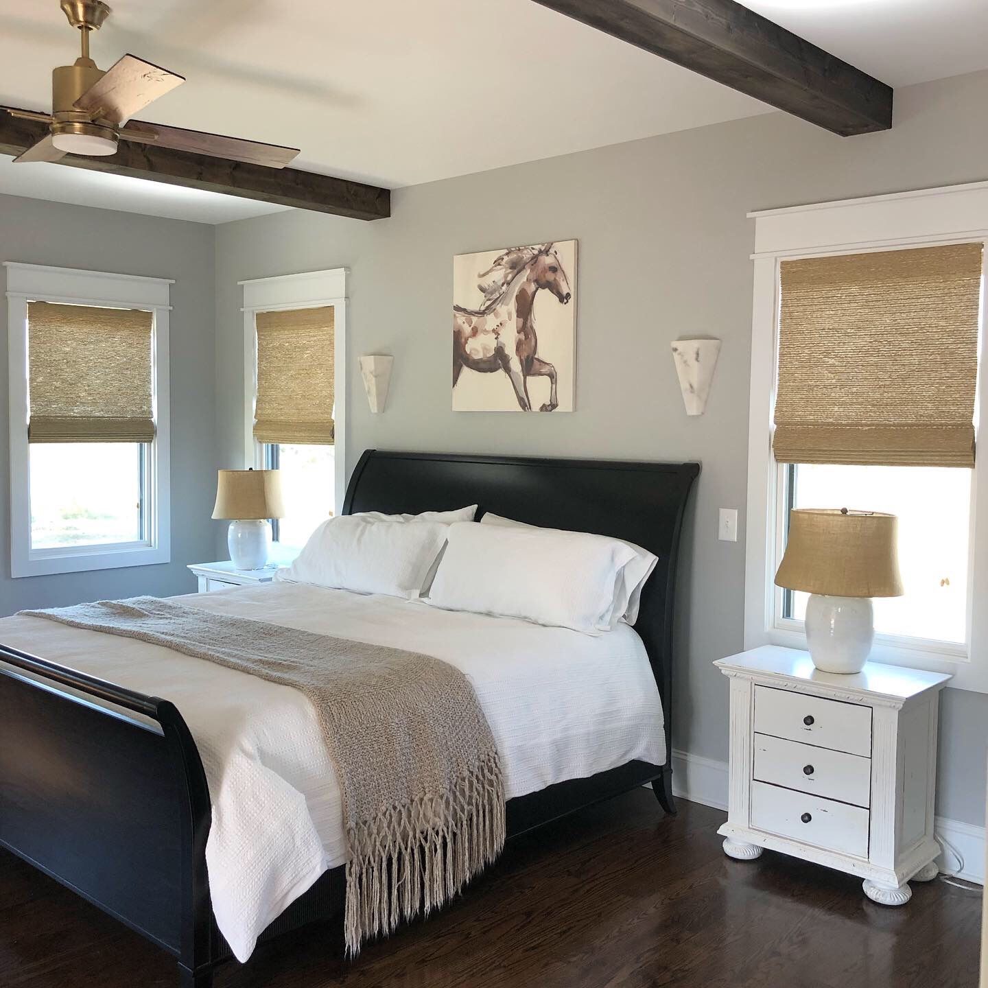 Bedroom with bed, nightstands, windows with shades, artwork, and ceiling fan. Light gray walls, dark wood trim.