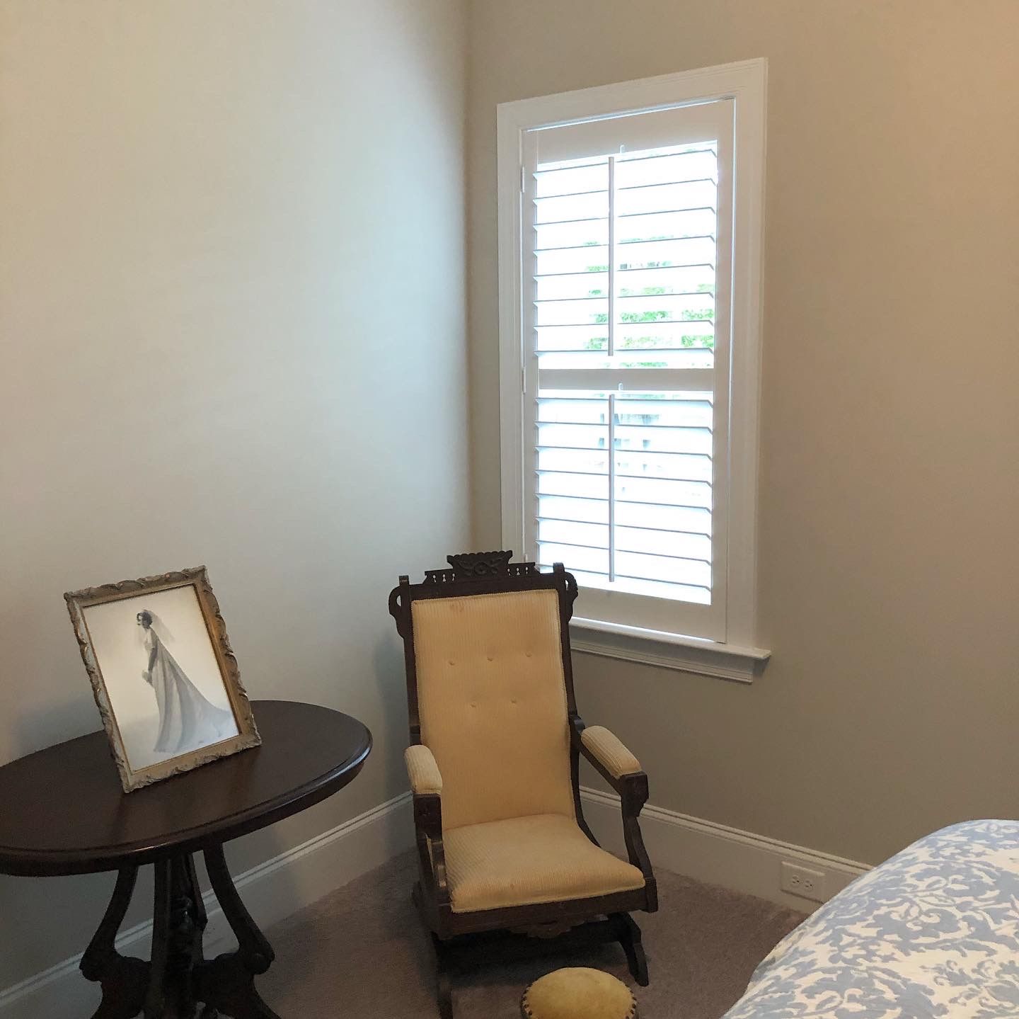 Room corner with small round table, antique chair, and shuttered window.