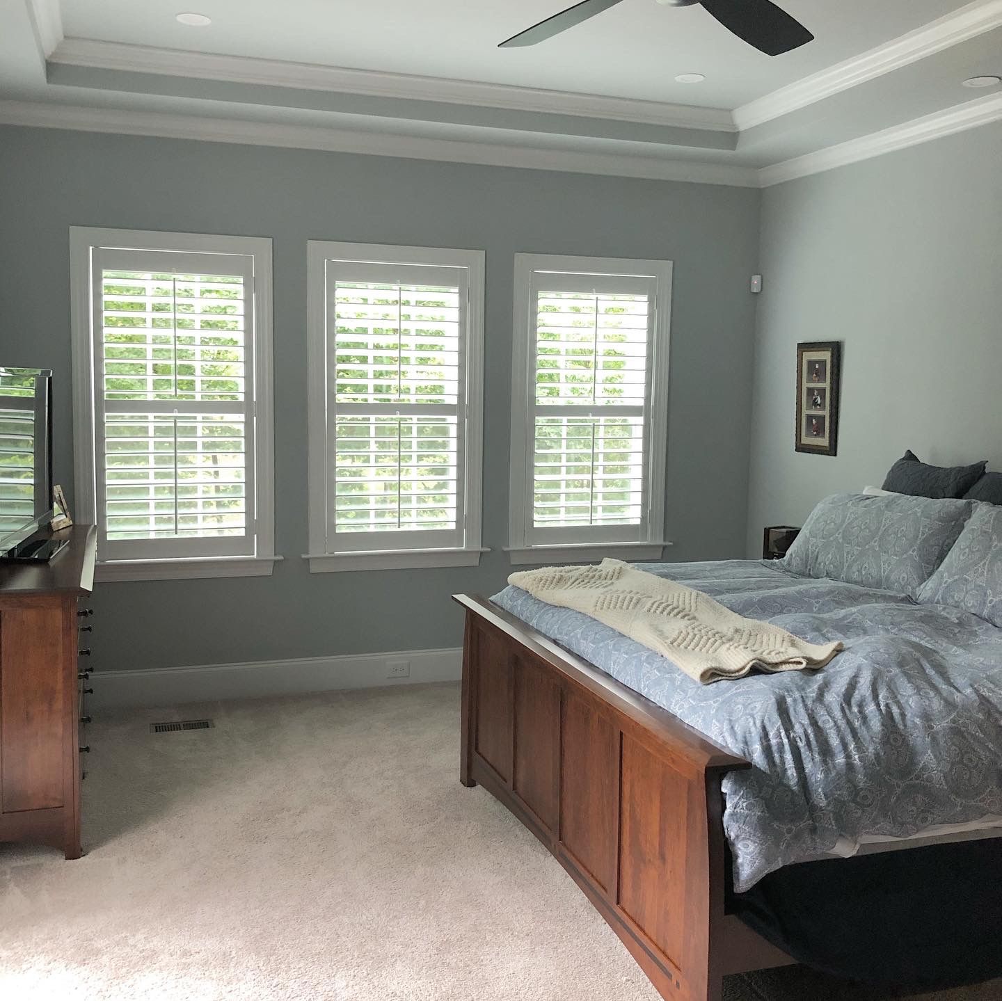 Bedroom with blue walls, three windows with white shutters, and a wooden bed.