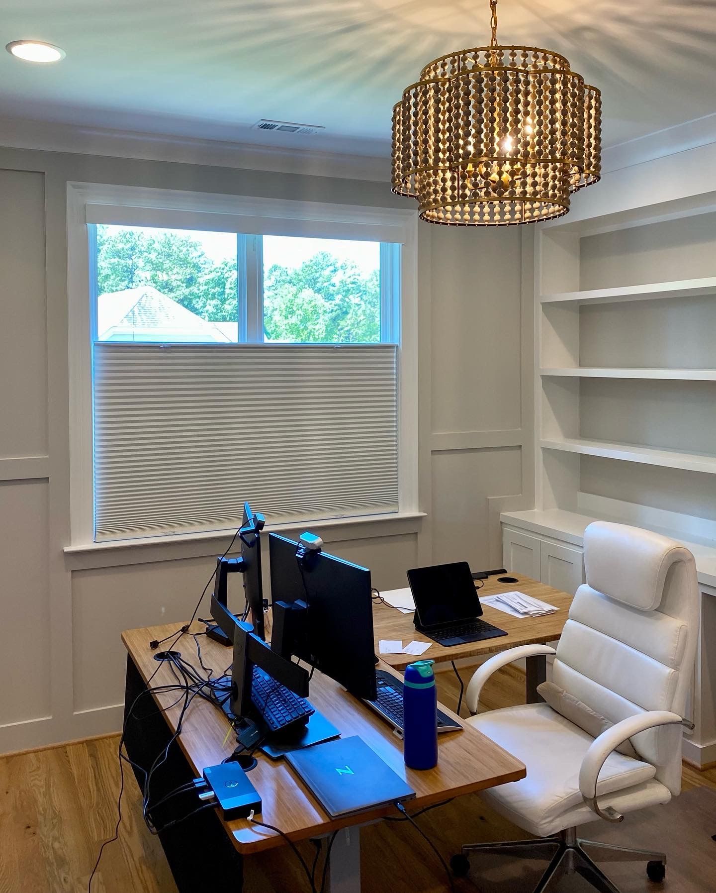 Home office with a desk, two monitors, laptop, white chair, and a decorative light fixture.