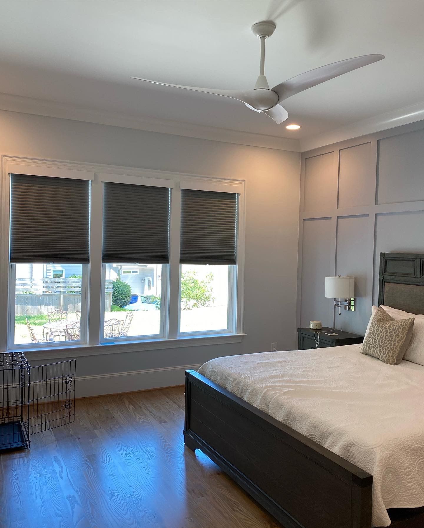 Bedroom with three windows, gray blinds, wooden floors, a bed, and a ceiling fan.