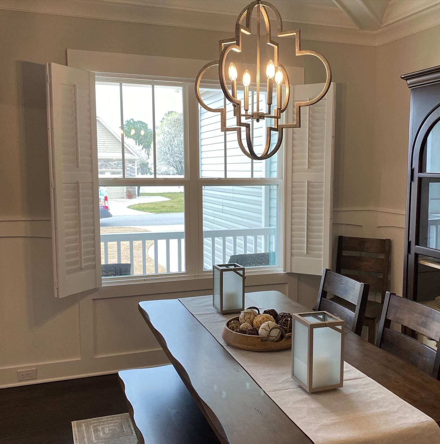 Dining room with a wooden table, window with shutters, and a chandelier.