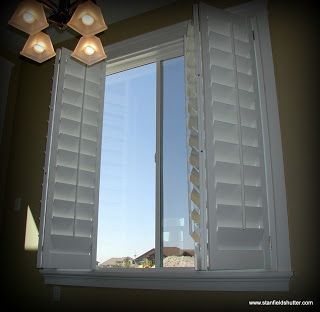 White shutters on an open window, revealing a blue sky and distant buildings.