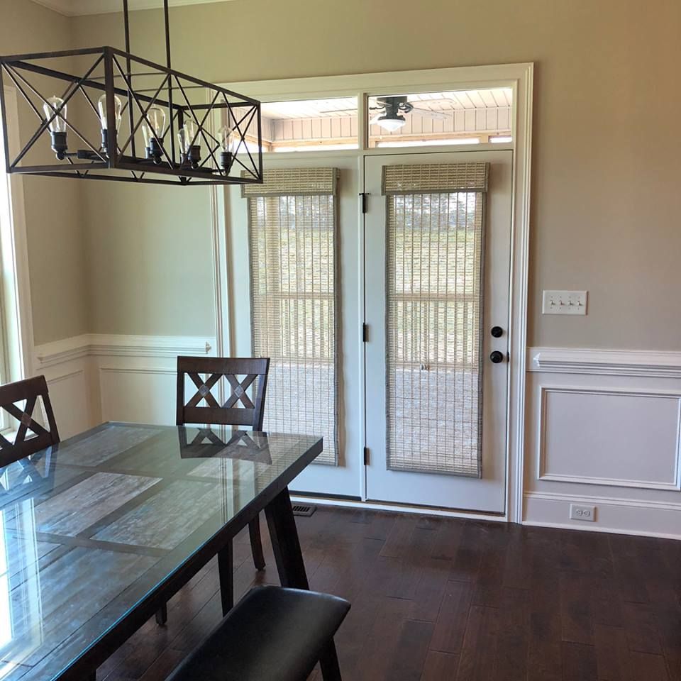 Dining room with table, chairs, chandelier, and French doors with shades; dark wood floors and neutral walls.