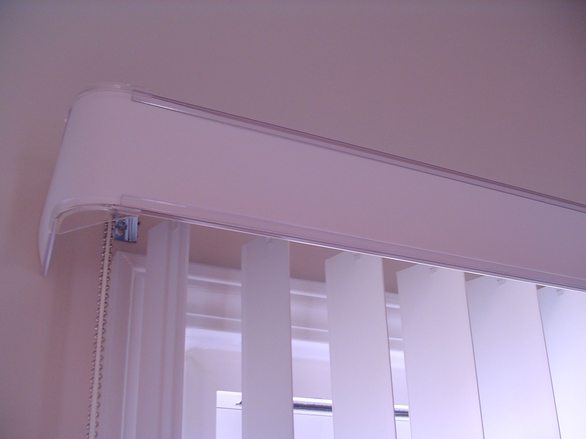 White vertical blinds installed near a window, with a curved valance at the top.