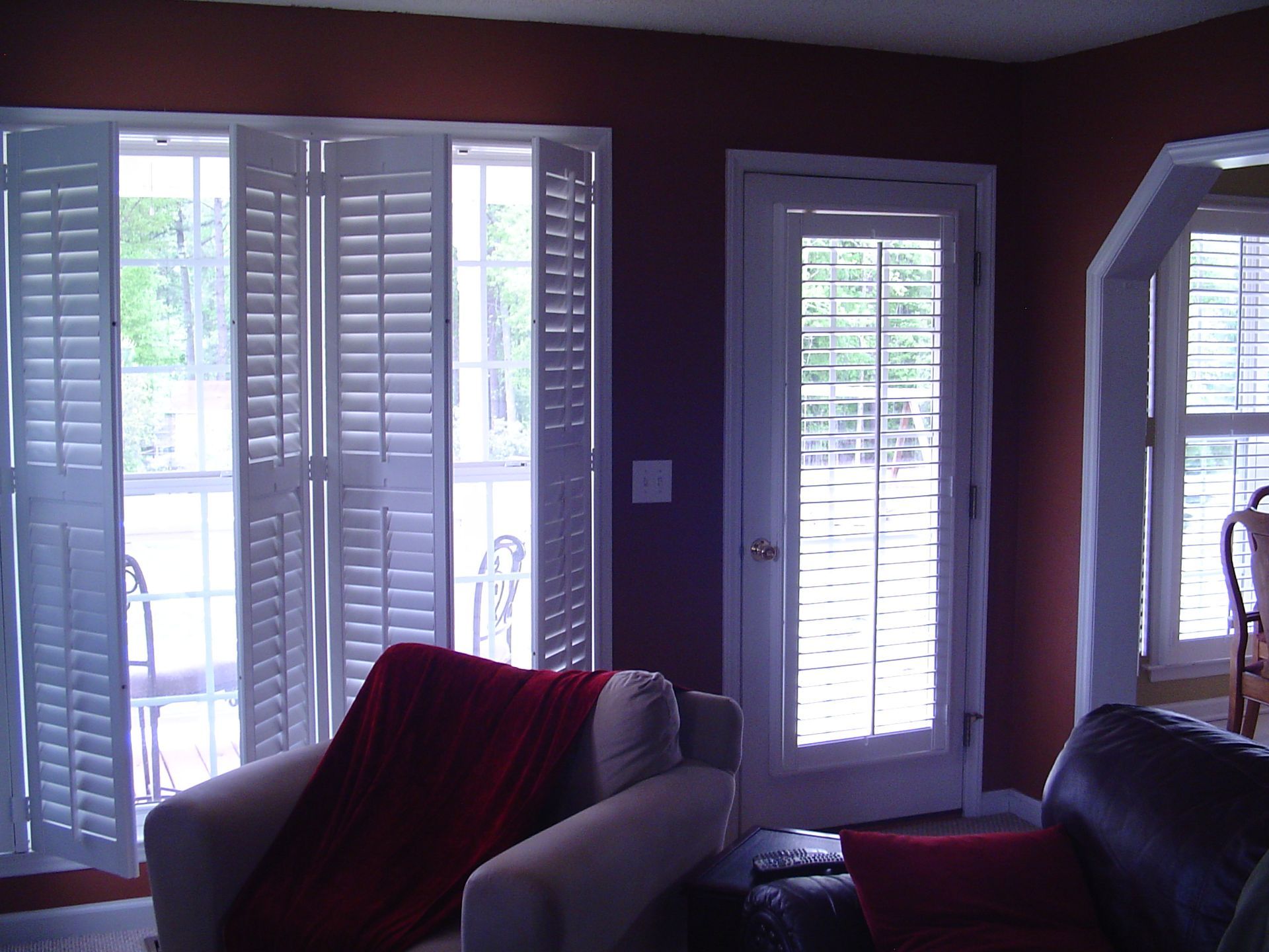 Interior room with white shutters on large windows and door, red accents, and two armchairs.