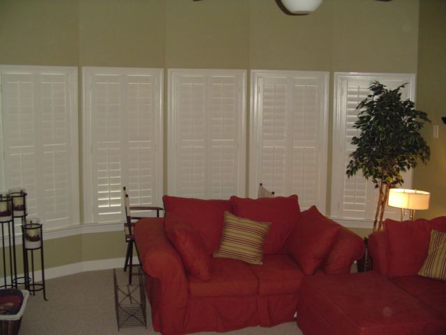 Living room with red sofa, white shutters, and a potted plant.