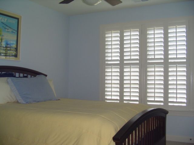 Bedroom with bed, blue walls, white shutters, and a framed picture.