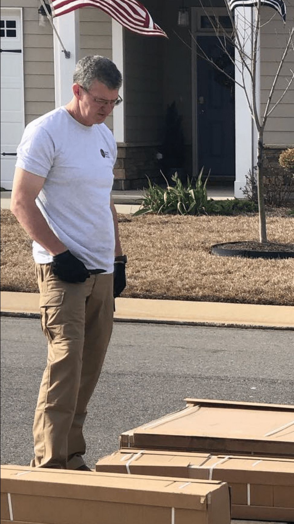 Man in casual clothes standing near cardboard boxes outdoors, looking down.