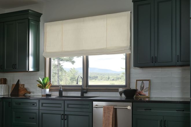Kitchen with dark green cabinets, a window with a beige Roman shade, and a view of a landscape.