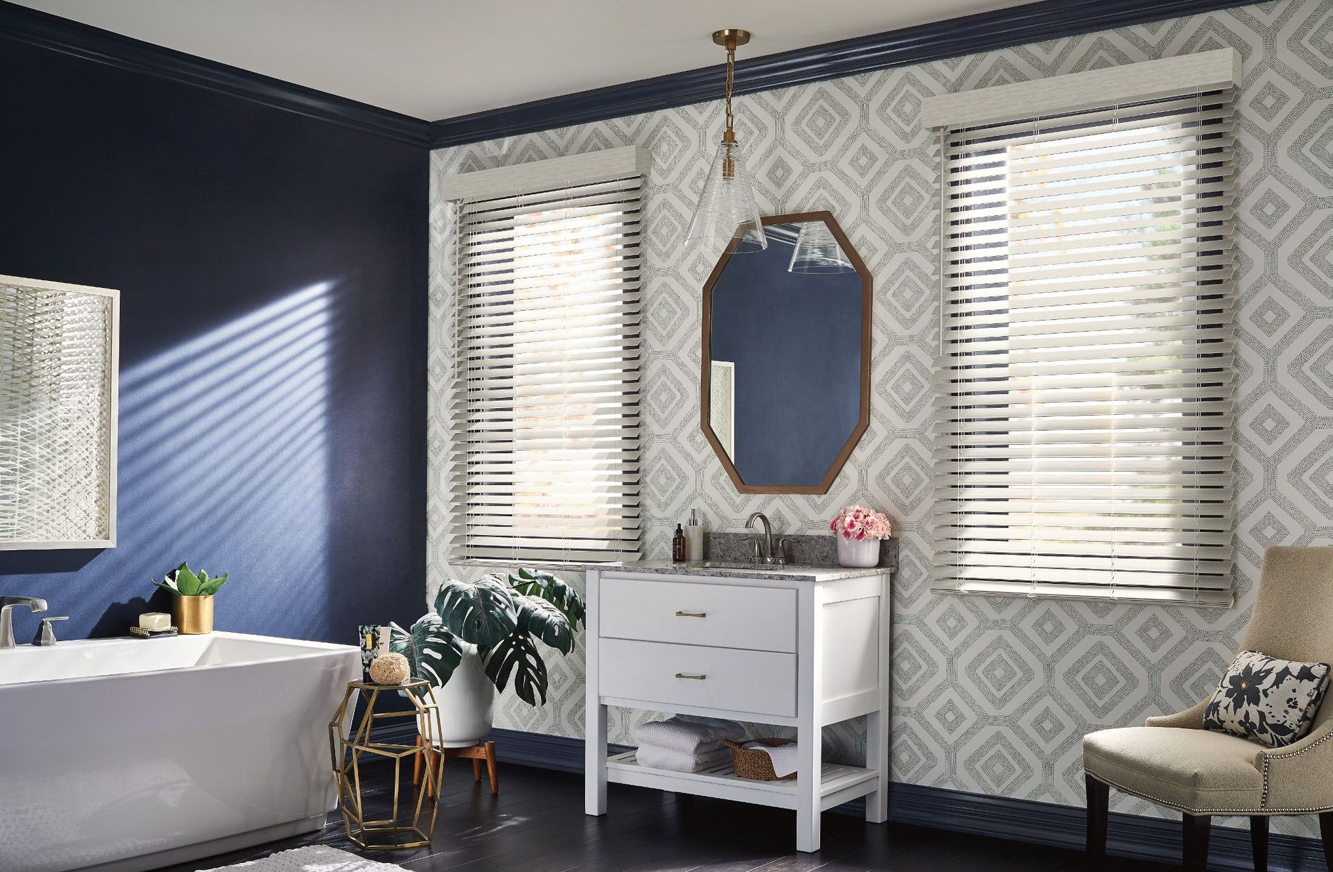 Bathroom with blue walls, patterned wallpaper, white vanity, bathtub, and windows with blinds.