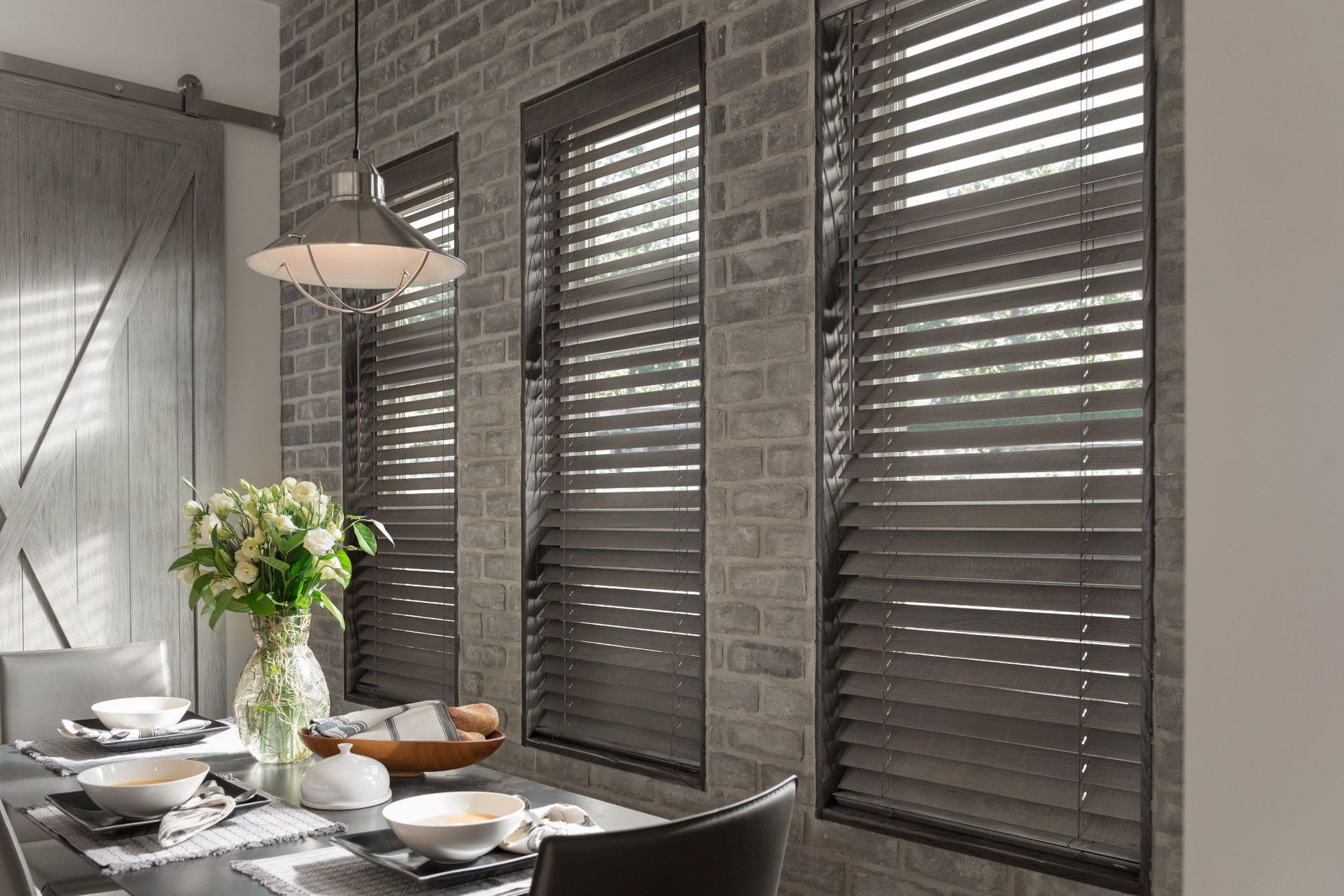 Dining room with gray brick wall, gray blinds, a table set for a meal, and overhead light.