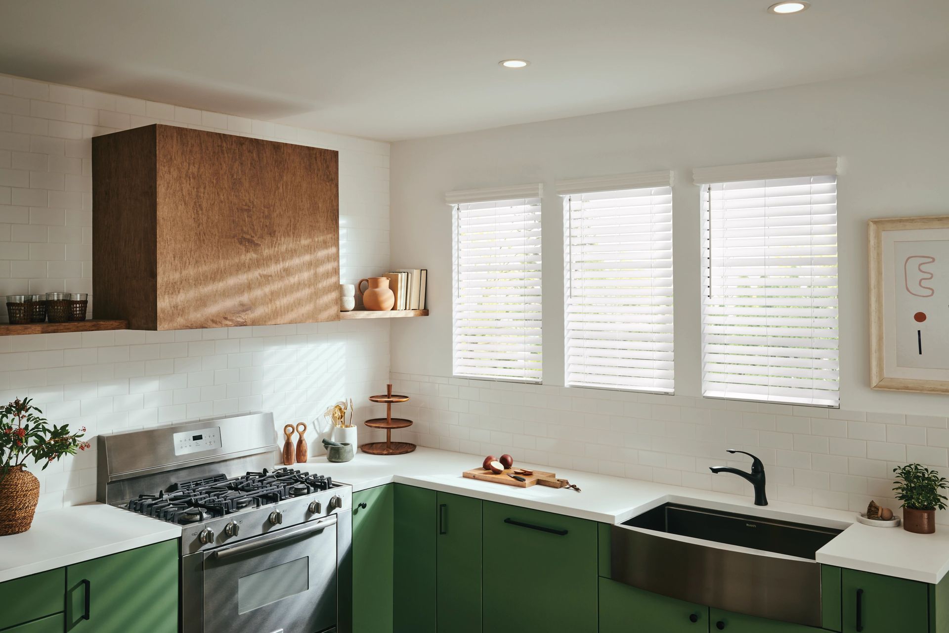 Green and white kitchen with stove, sink, and wood-paneled vent hood. Three windows with blinds.