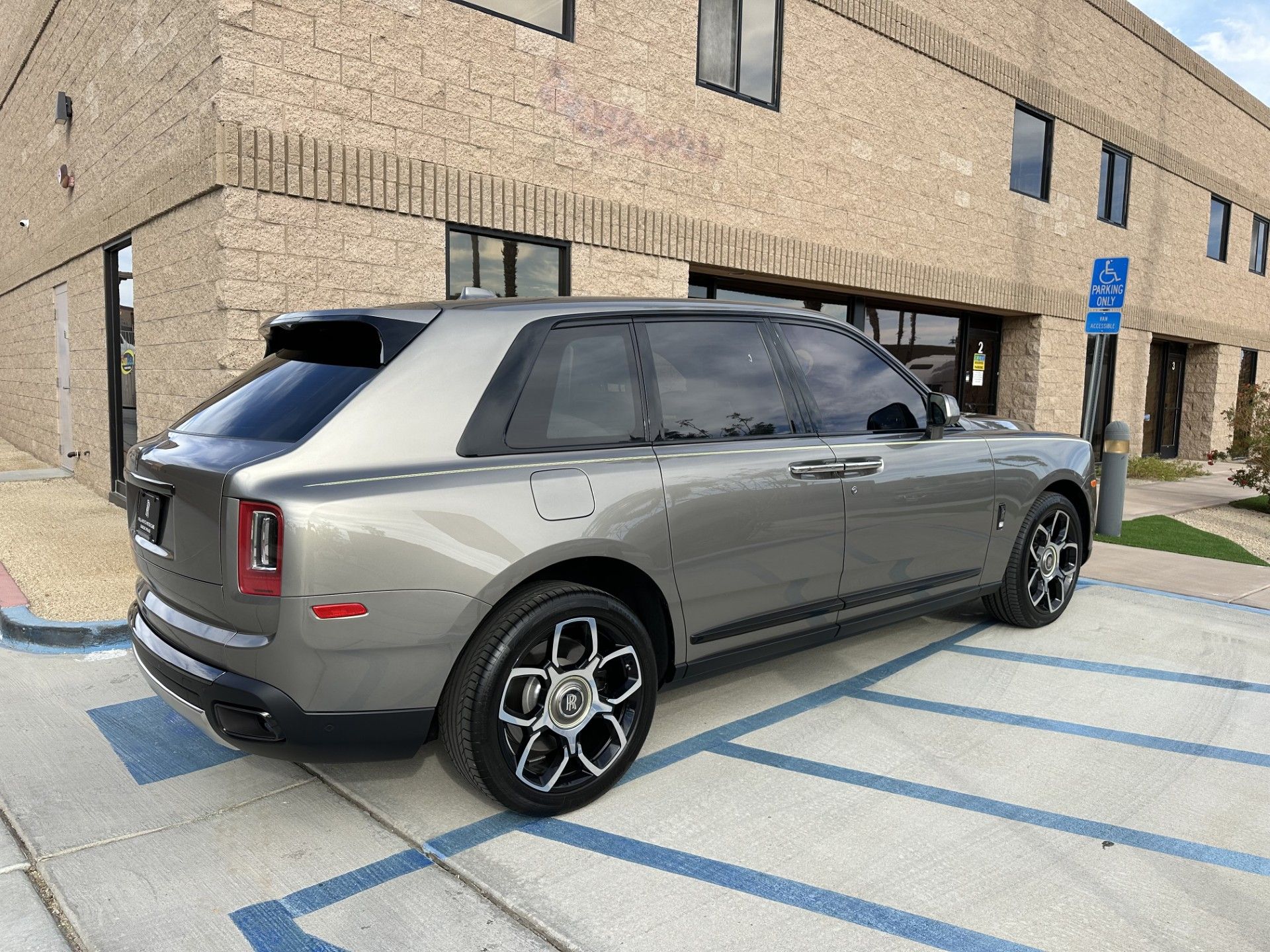 A gray car is parked in a handicapped parking spot in front of a brick building.