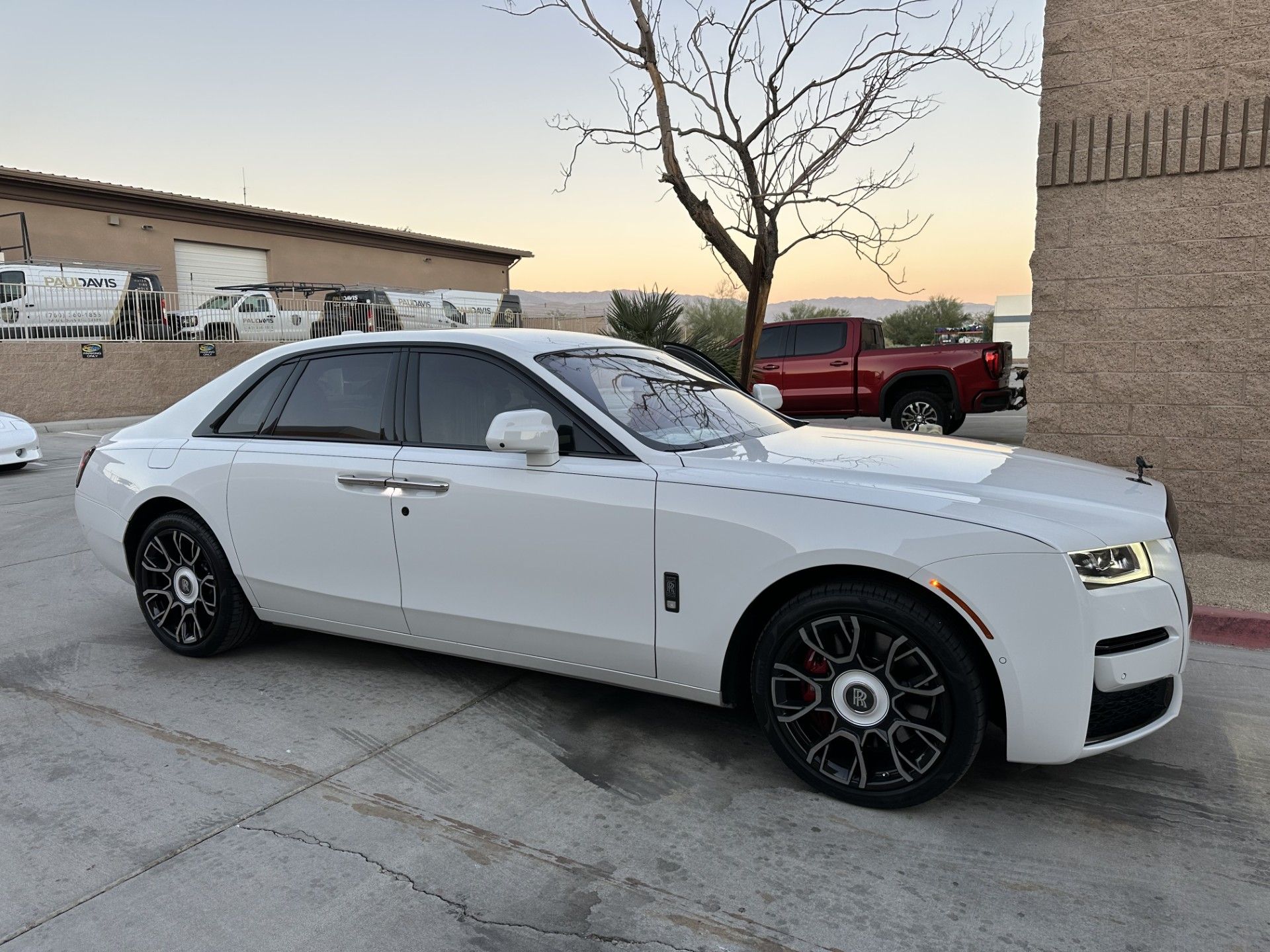 A white rolls royce ghost is parked in front of a building.
