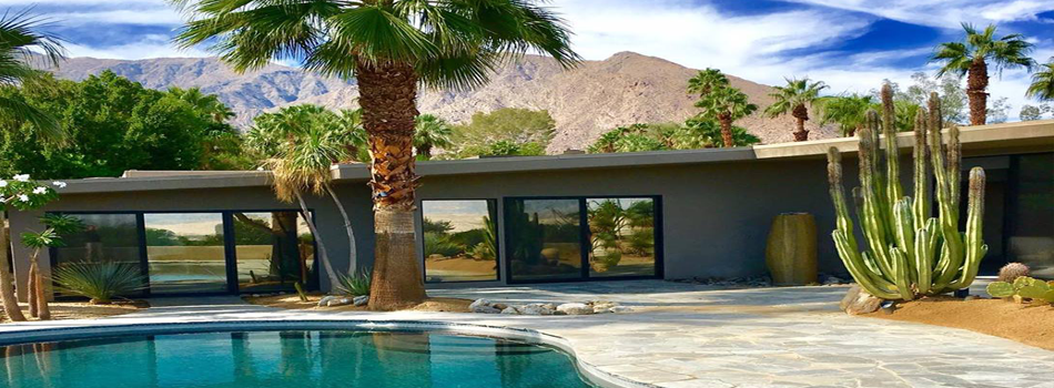 A swimming pool in front of a house with palm trees and mountains in the background.