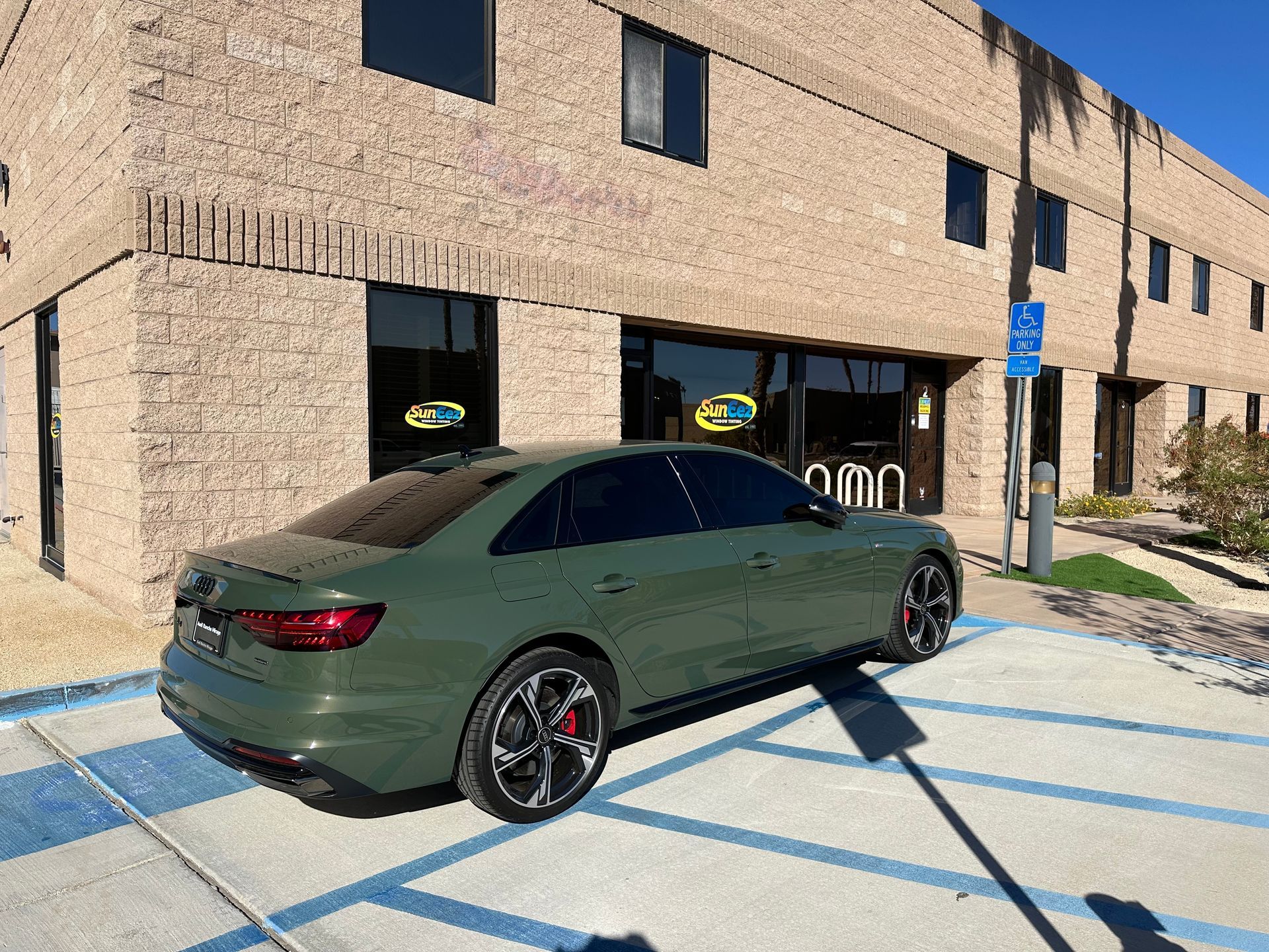 A green car is parked in a handicapped parking spot in front of a building.