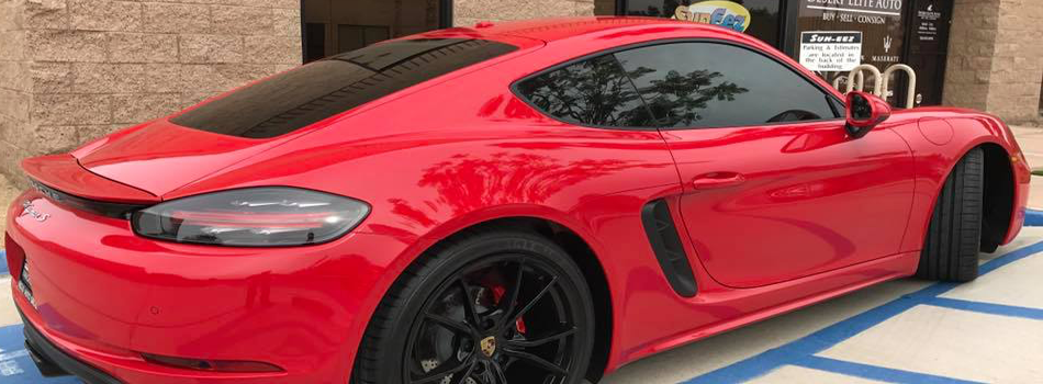 A red porsche boxster is parked in a handicapped parking spot in front of a building.