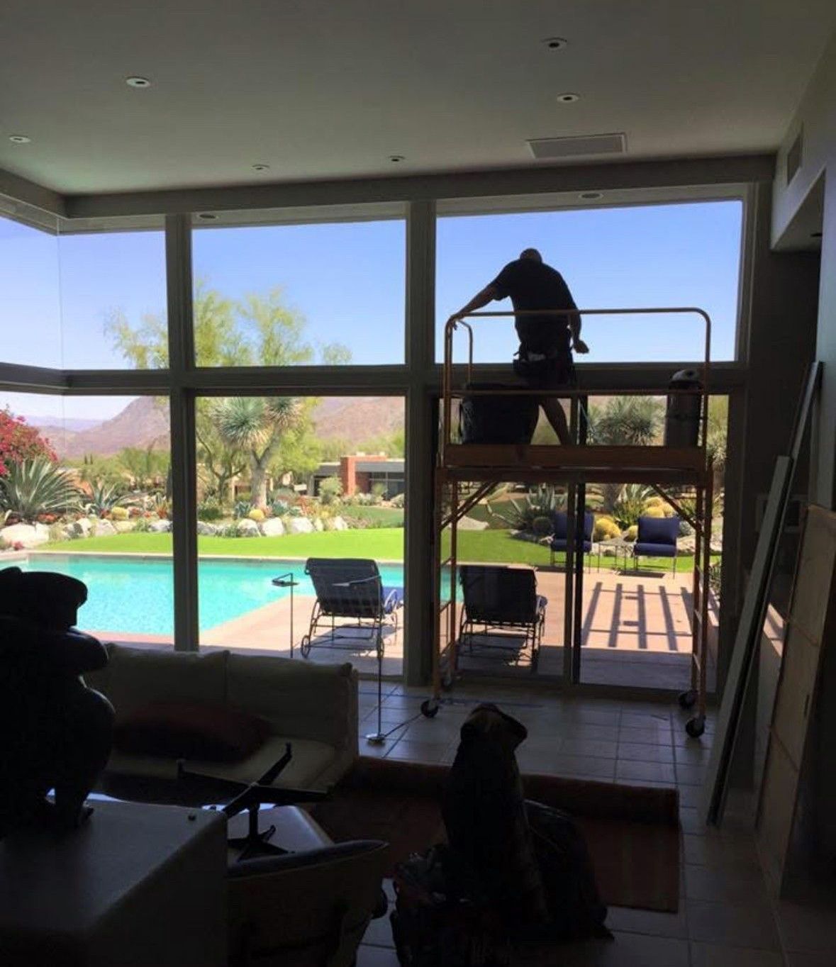 A man is standing on a scaffolding in front of a large window.