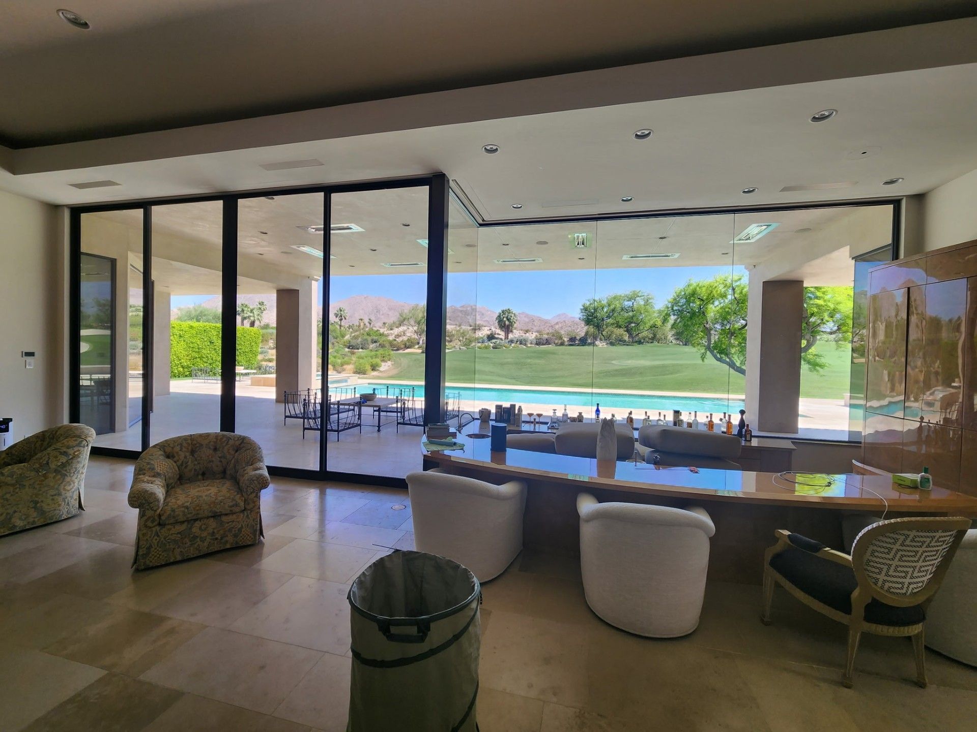 A living room with chairs , a desk , and a large window overlooking a pool.