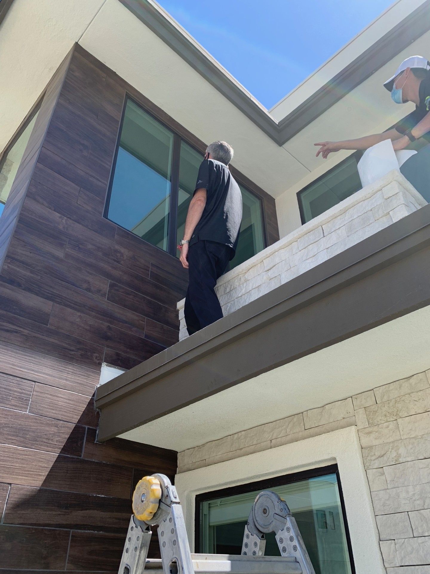 A man is standing on the roof of a building next to a ladder.