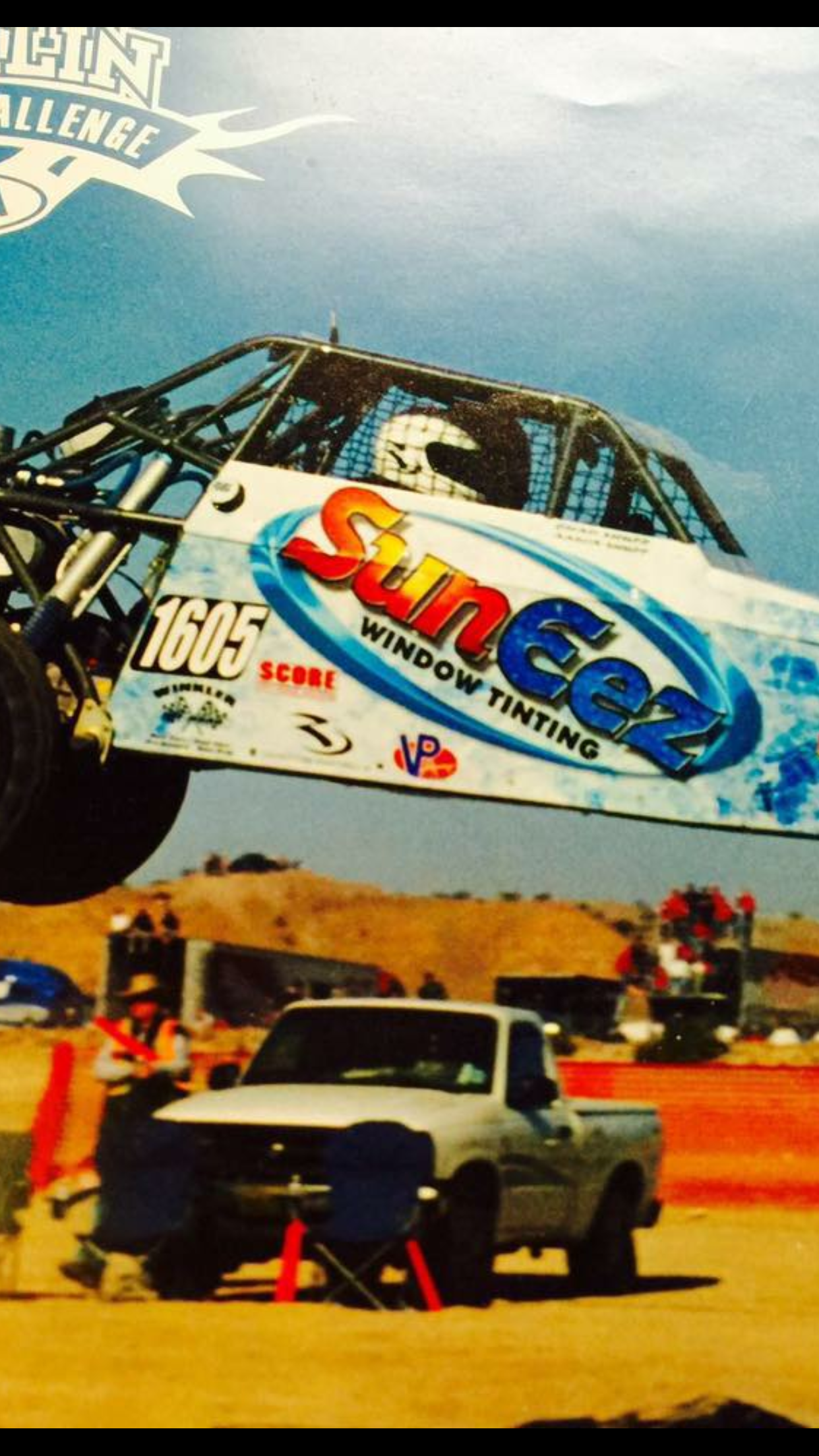 A white truck is parked in front of a monster truck that says SunEez