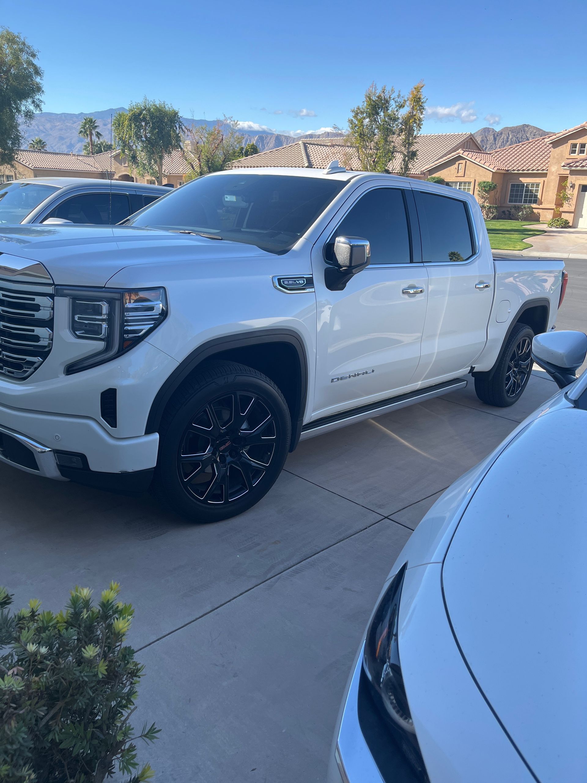 A white truck is parked in a driveway next to a white car.