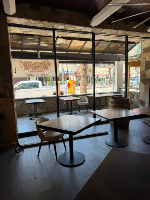 Empty café interior with dark tables and chairs, large windows, and street view outside
