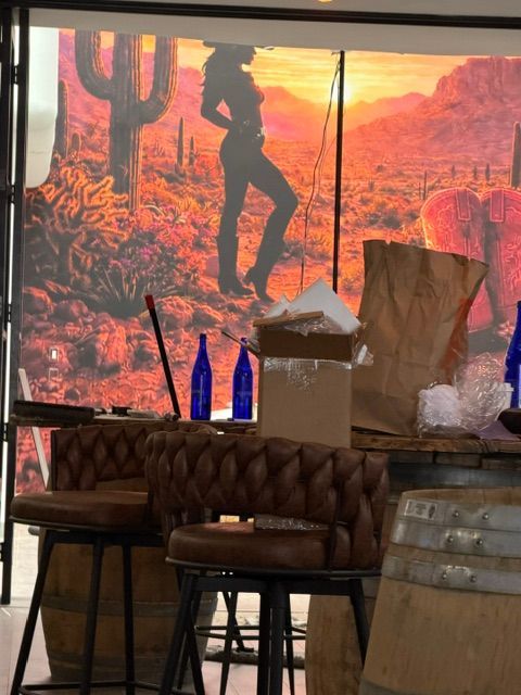 Desert-themed restaurant interior with cactus mural, tufted chairs, blue bottles, and a lit lamp on a table