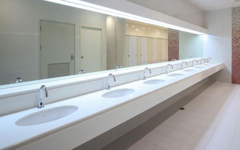 Bright public restroom with long white sink counter, mirrors, and stalls in a clean tiled interior.