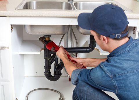 Plumber repairing sink pipes under a kitchen sink with a wrench