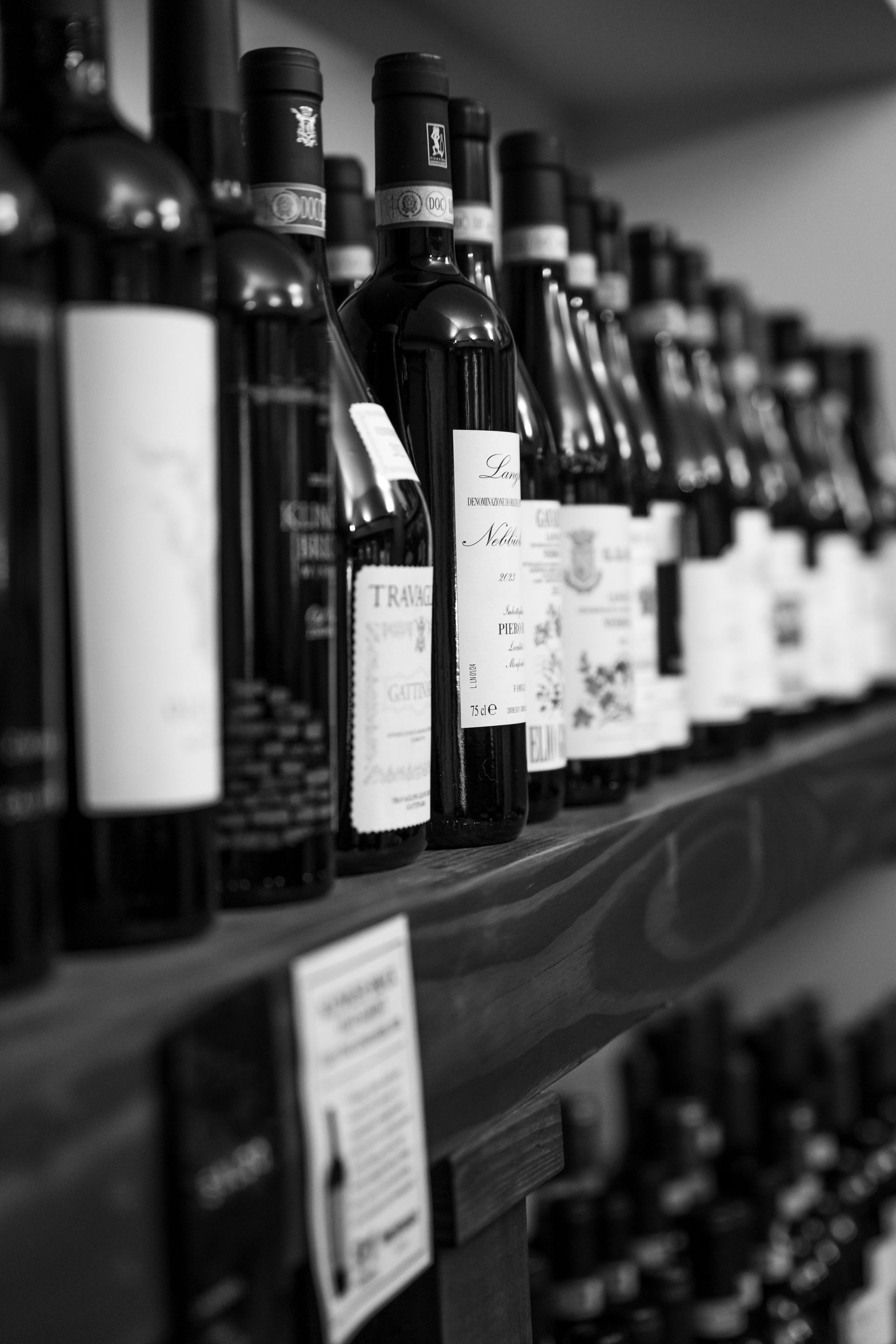 Black and white photo of wine bottles on a wooden shelf in a store.