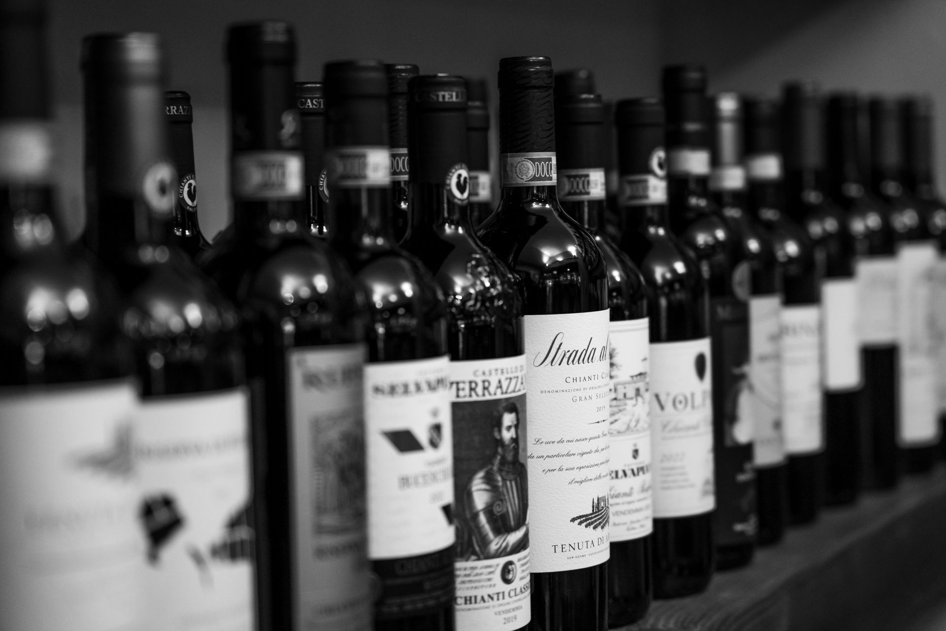 Row of wine bottles with labels, in black and white.