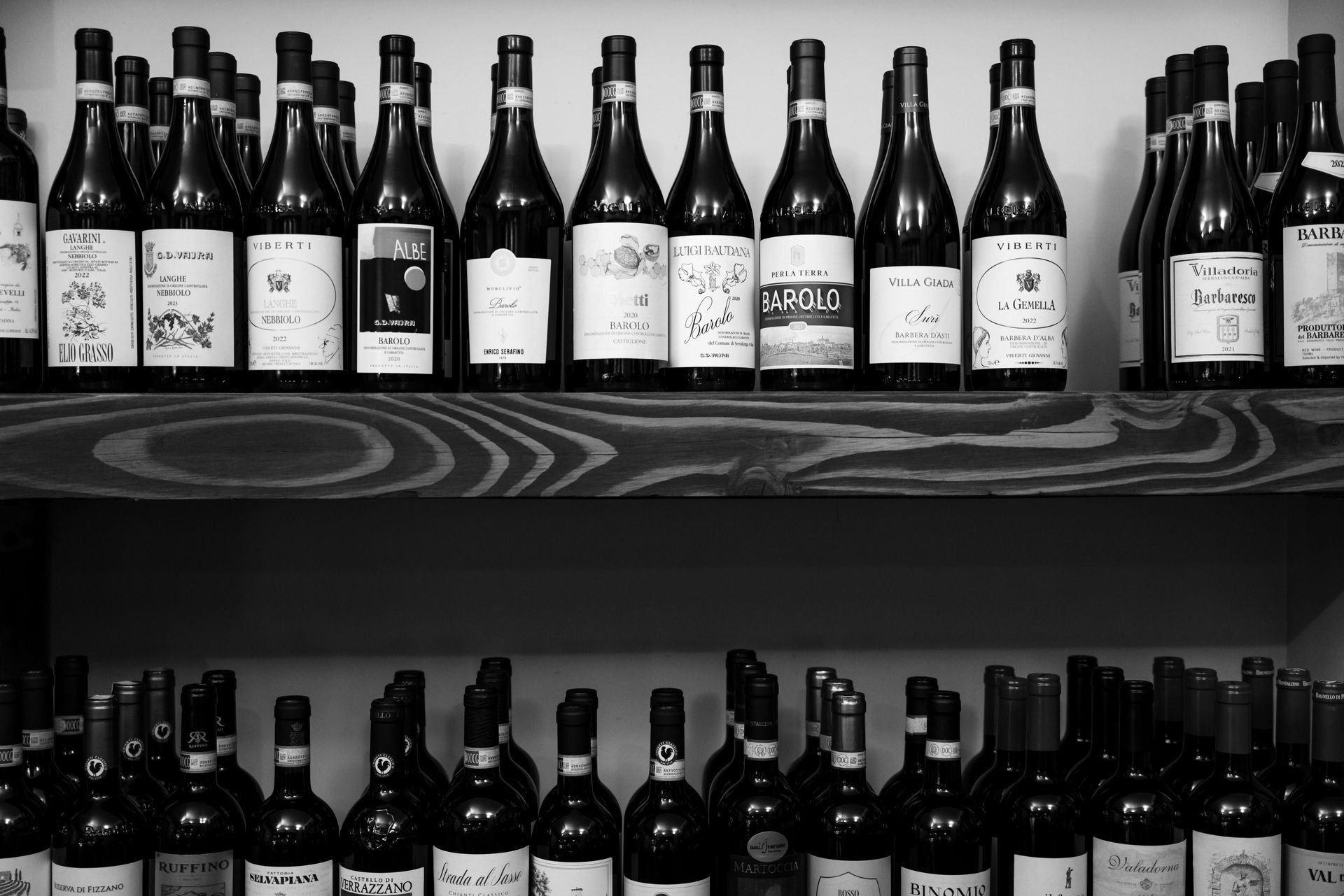 Rows of wine bottles on wooden shelves, black and white.