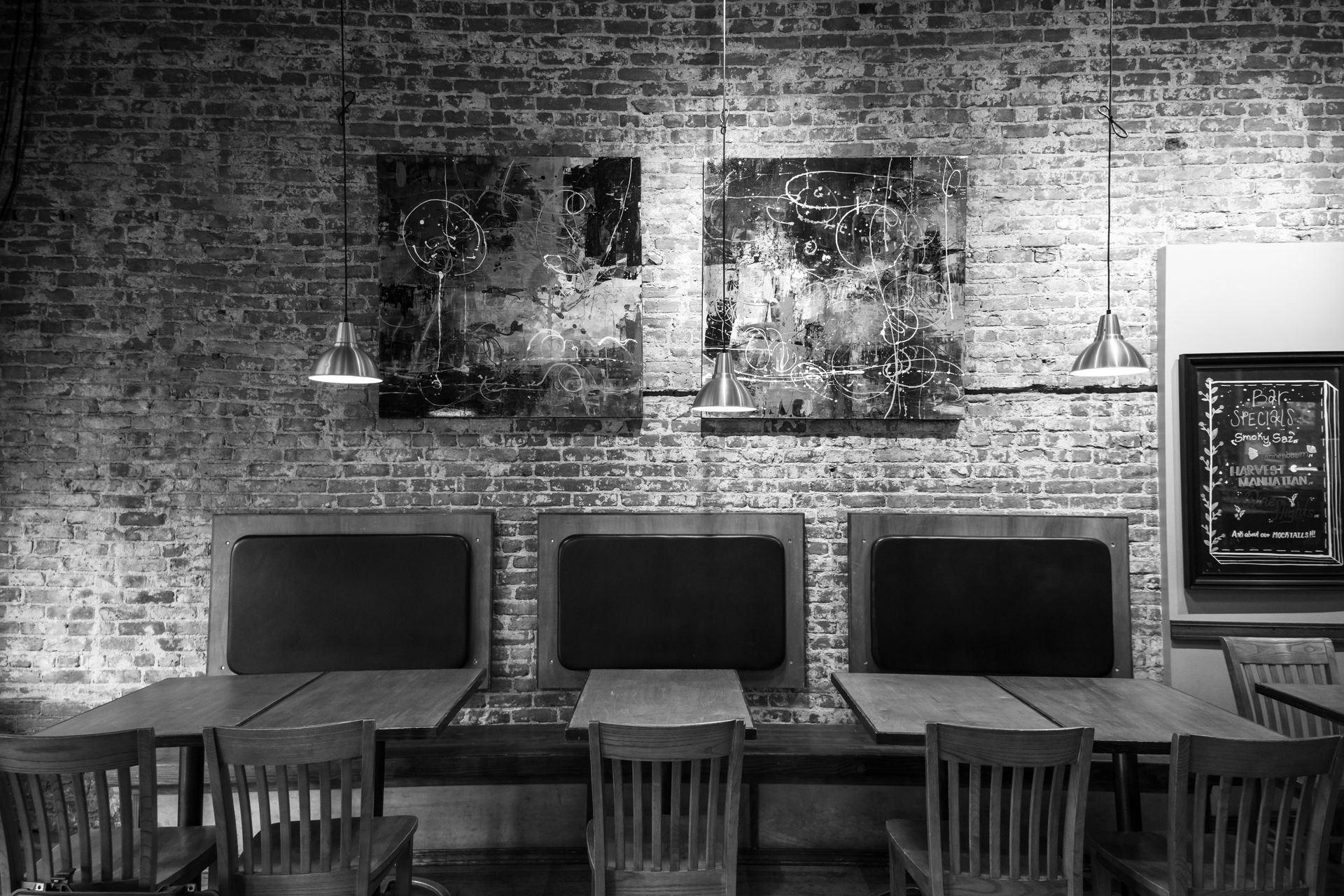 Black and white cafe interior with exposed brick, abstract art, tables, chairs, and two hanging lights.