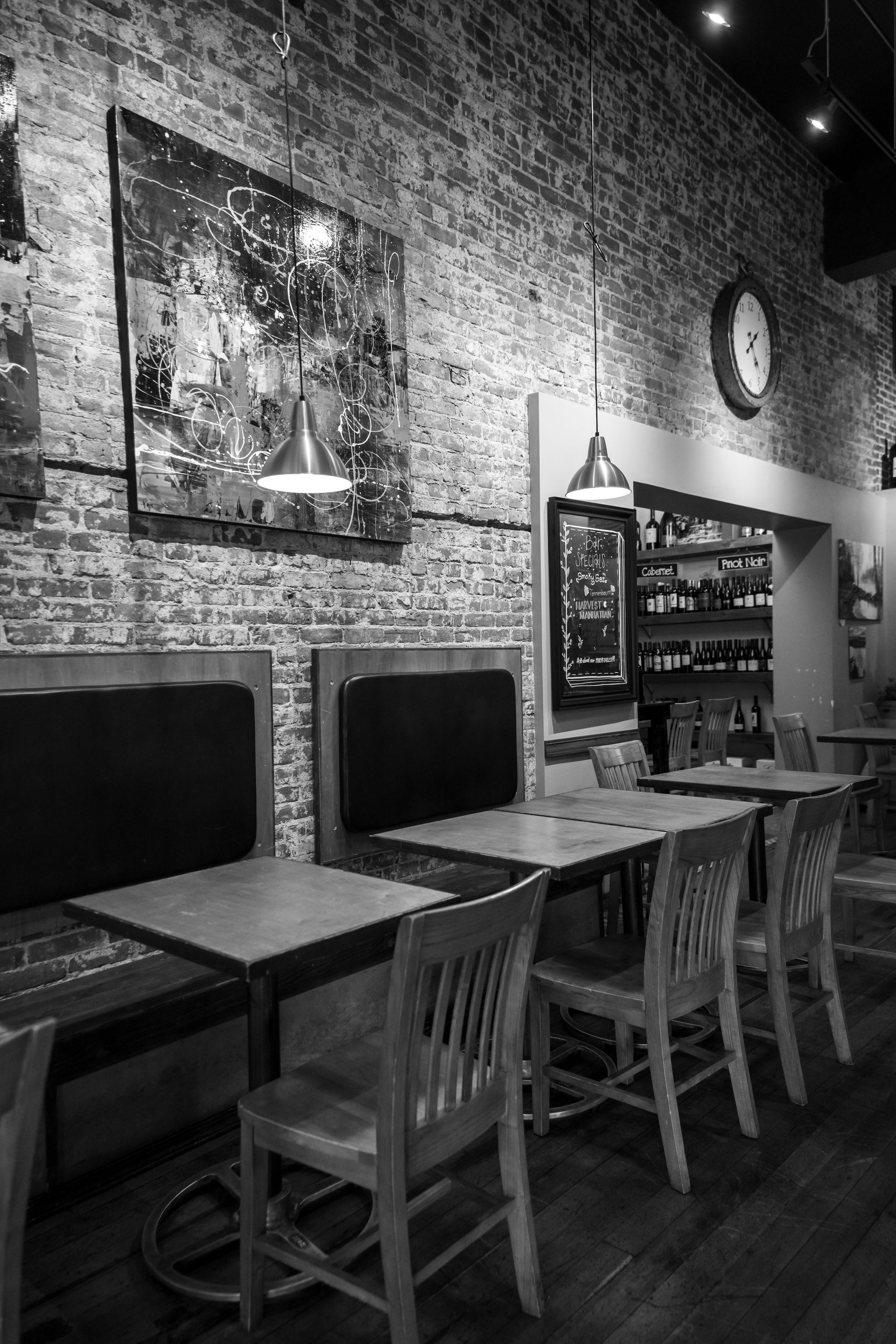 Black and white photo of a restaurant interior with tables, chairs, brick walls, and artwork.