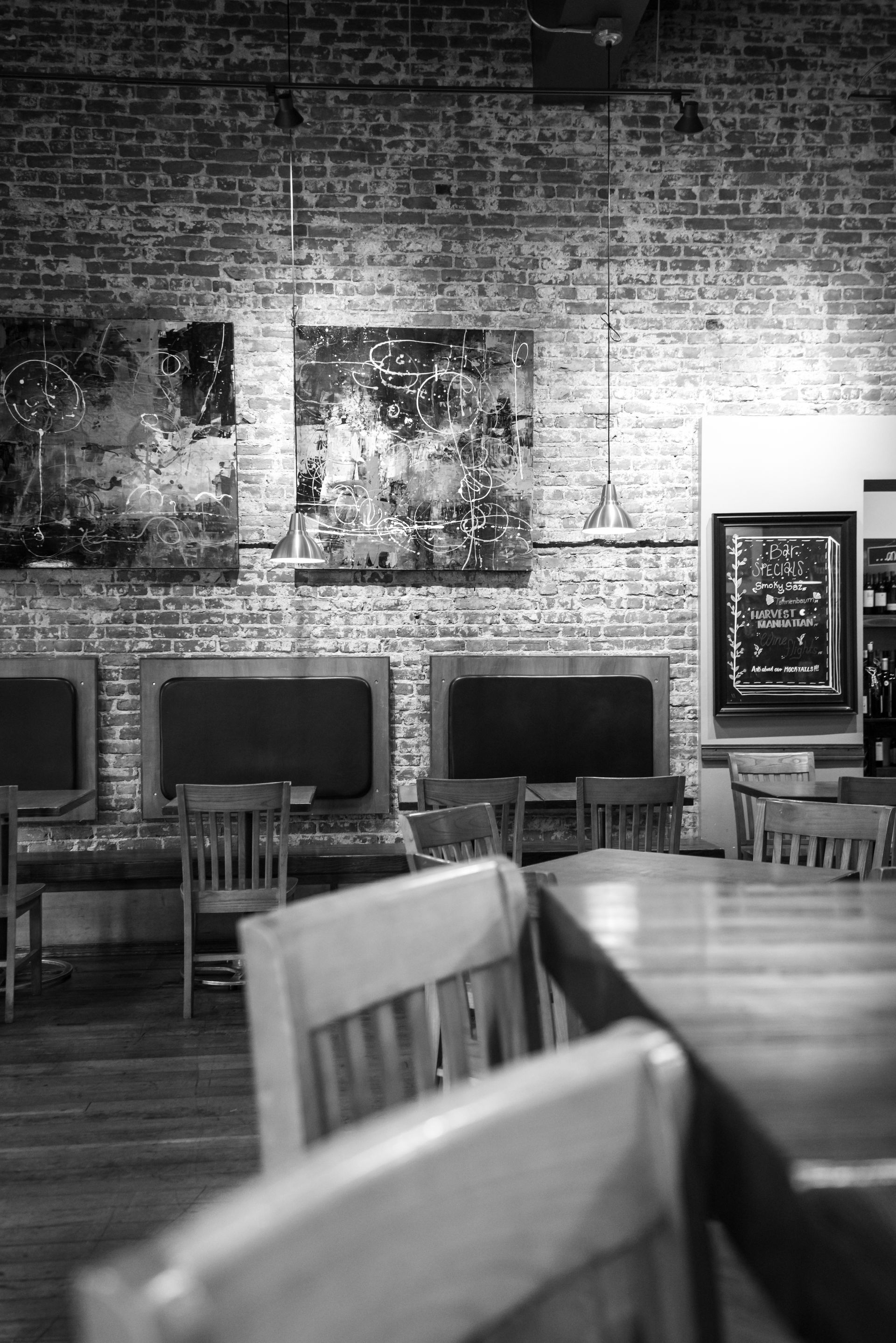 Interior of a restaurant with exposed brick walls, artwork, tables, and wooden chairs.