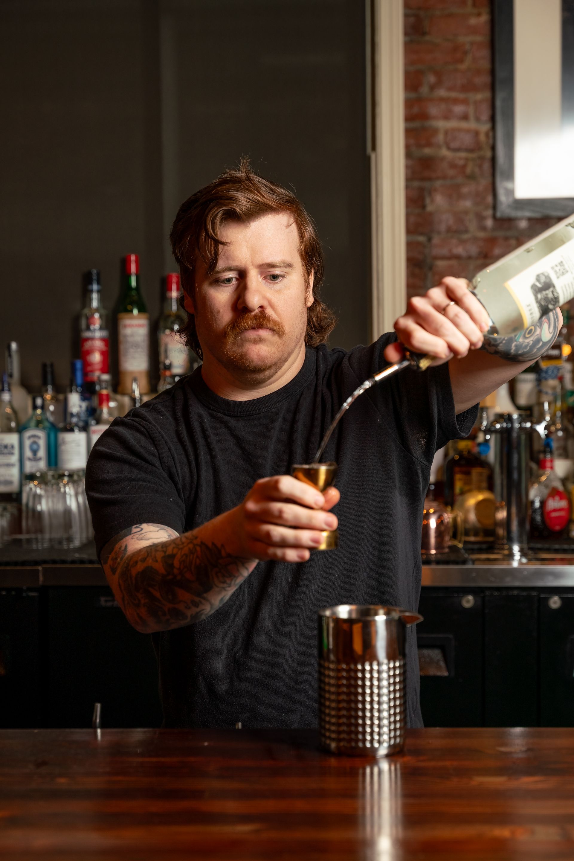 A bartender pouring a liquid from a bottle into a jigger at a bar.