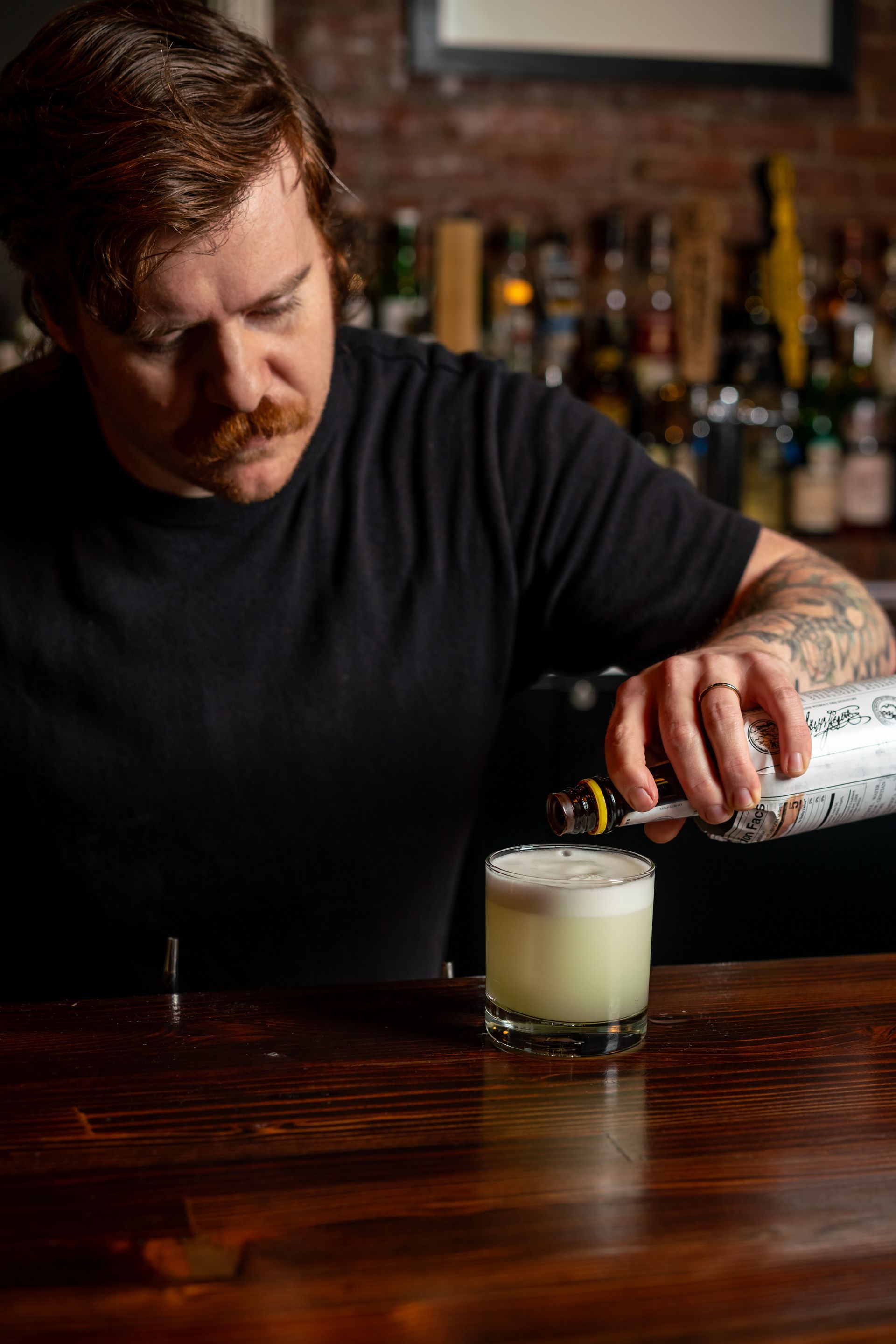 Bartender pouring a drink into a rocks glass on a wooden bar.