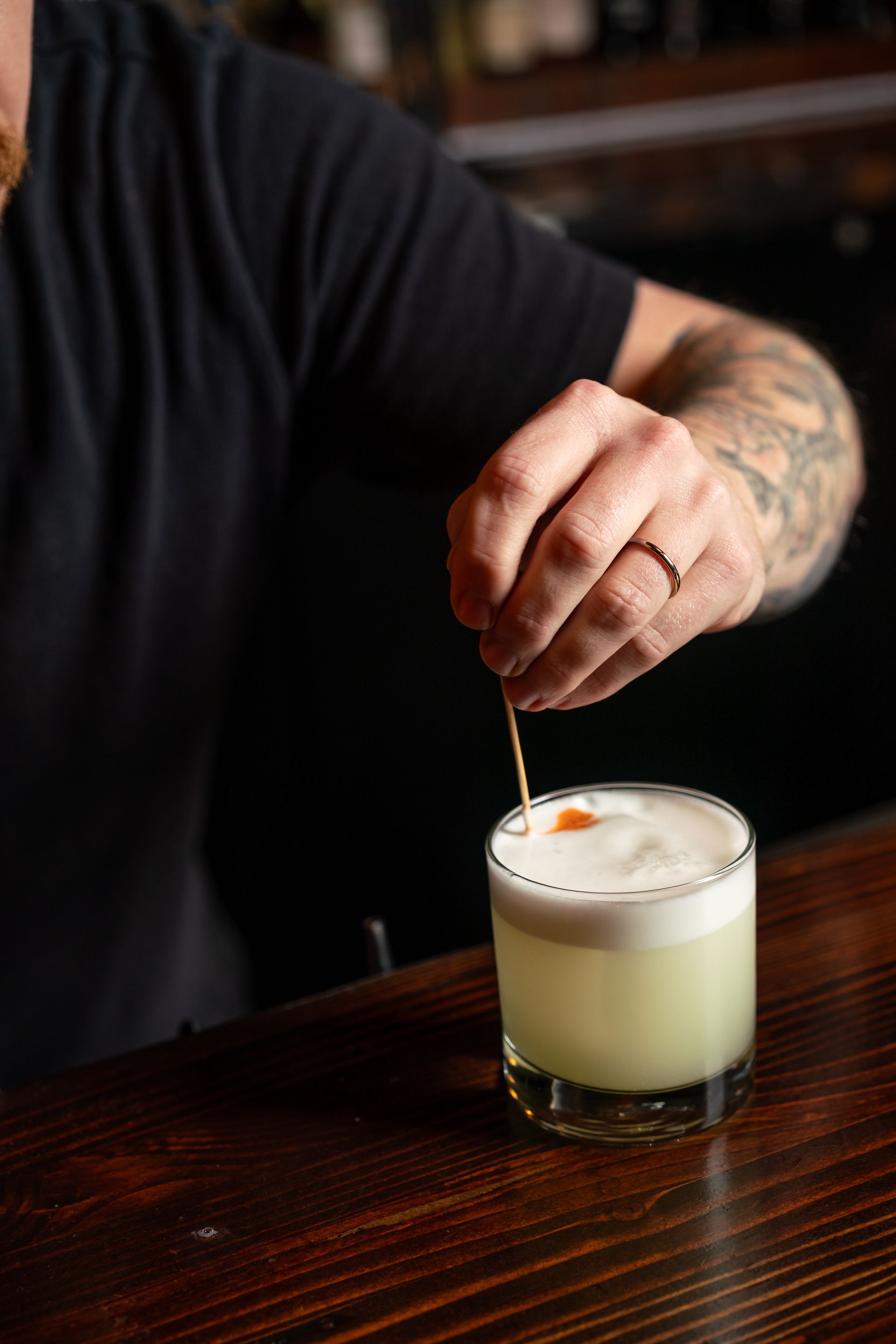 Bartender garnishing a cocktail with orange zest on a wooden bar.
