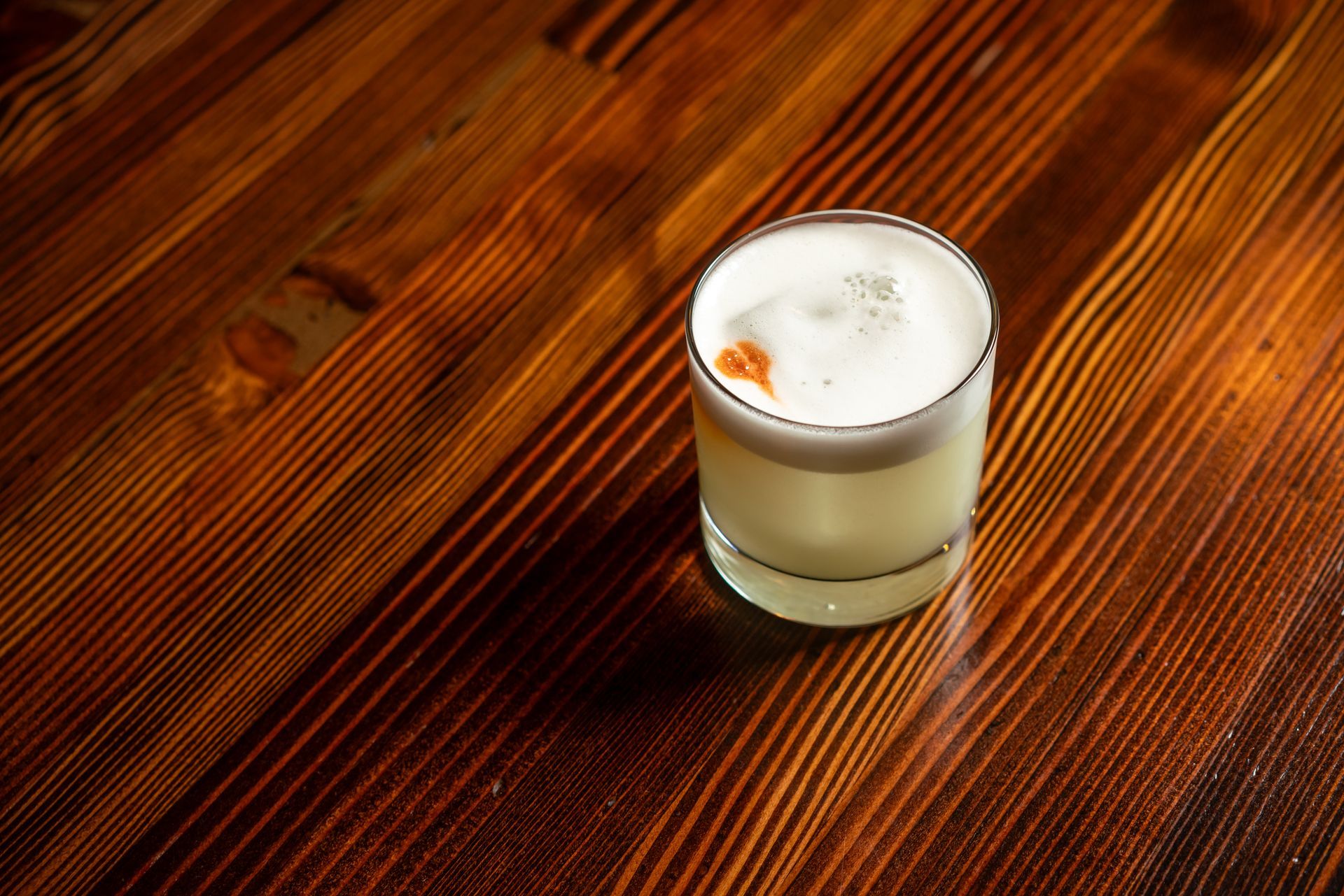 Cocktail with foamy top, on a dark wooden table.