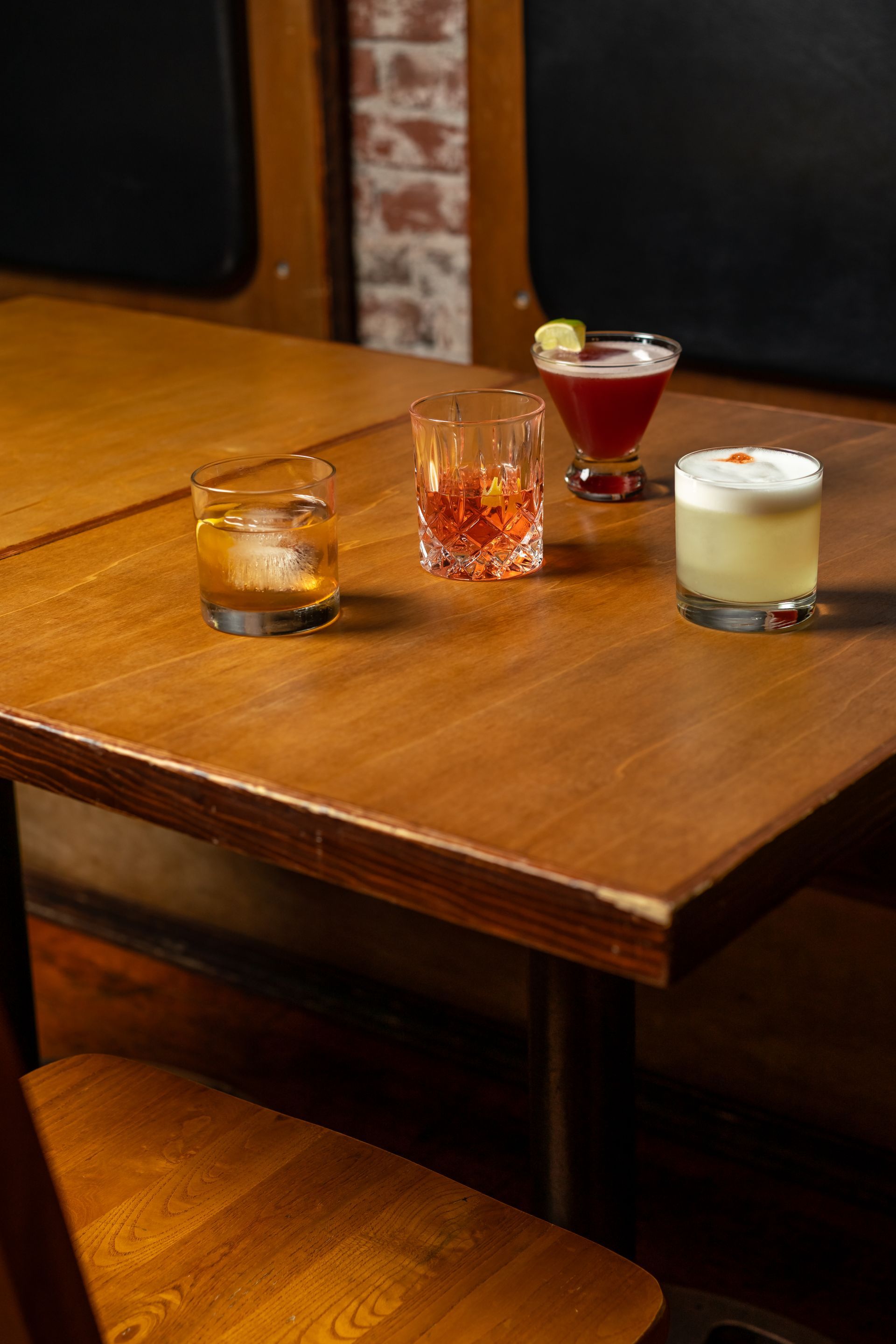 Four cocktails on a wooden table in a dimly lit bar setting.