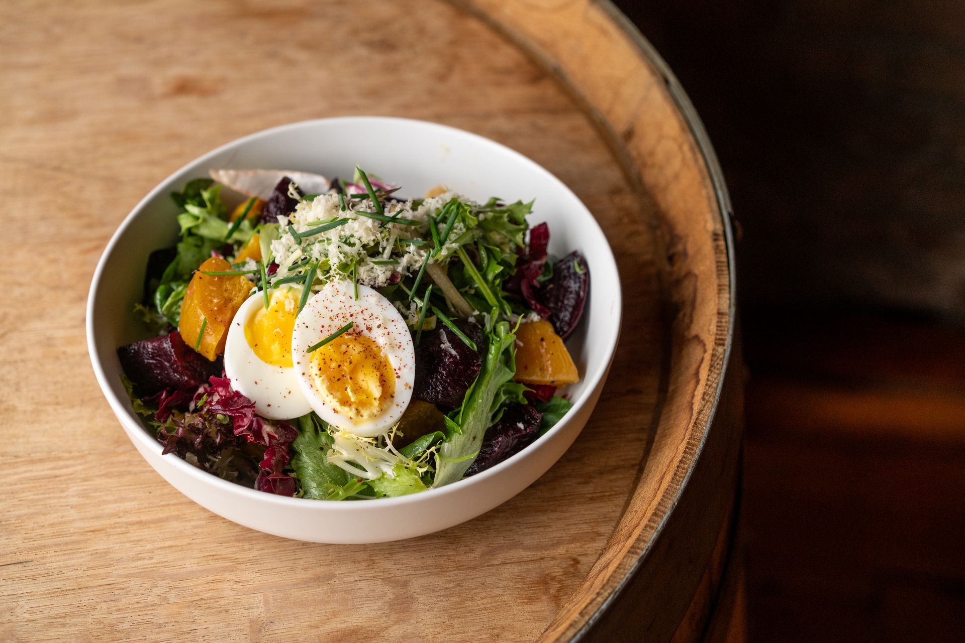 Salad bowl with egg, beets, orange slices, greens, and cheese, on a wooden surface.