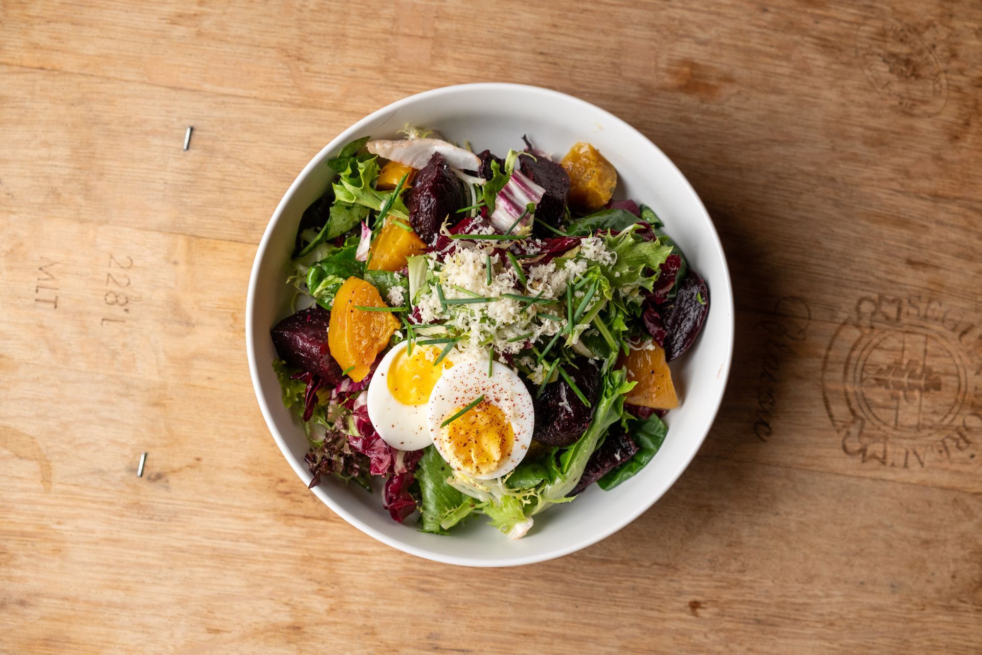 Salad with beets, egg, orange slices, and greens in a white bowl on a wooden surface.